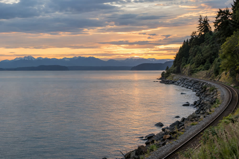The Puget Sound shoreline at University Place at sunset, a railway along the water and the Olympic Mountains beyond