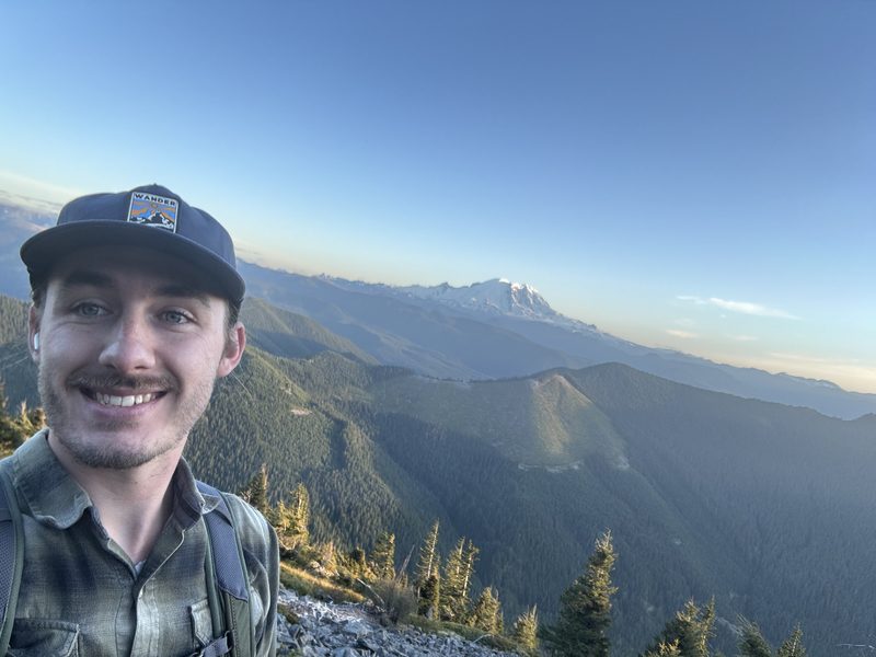 Jason, owner of Elliott Electric, on a ridge with Mount Rainier behind him