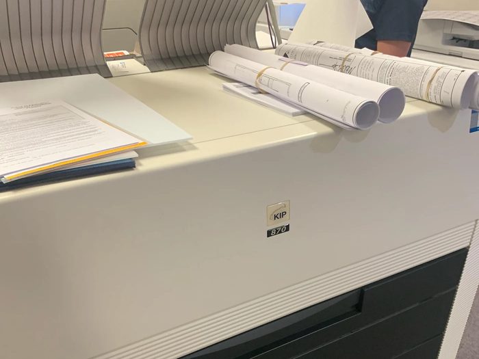 A KIP 870 wide-format printer in a customer's office, rolled drawings on top